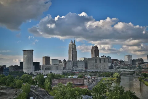 cleveland-oh Cleveland skyline featuring Key Tower and Terminal Tower with Cuyahoga River in the foreground under dramatic clouds.