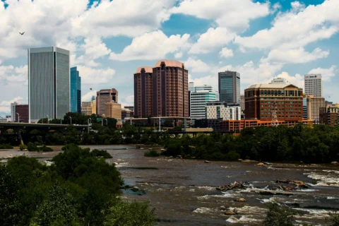 richmond-va Richmond, Virginia skyline with modern and historic buildings along the James River on a partly cloudy day.