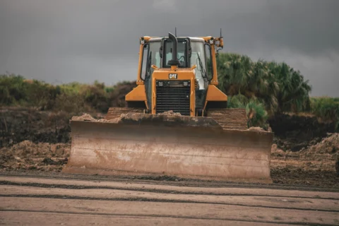 heavy-equipment Yellow Caterpillar bulldozer grading soil at a construction site under an overcast sky