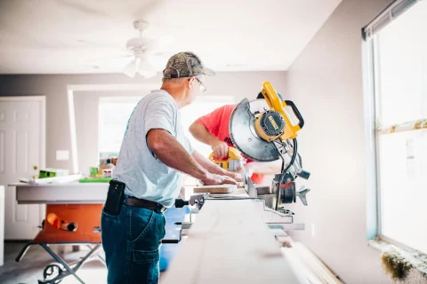 home-repair Contractors cutting lumber on a sliding compound miter saw inside a living room during home repair renovation