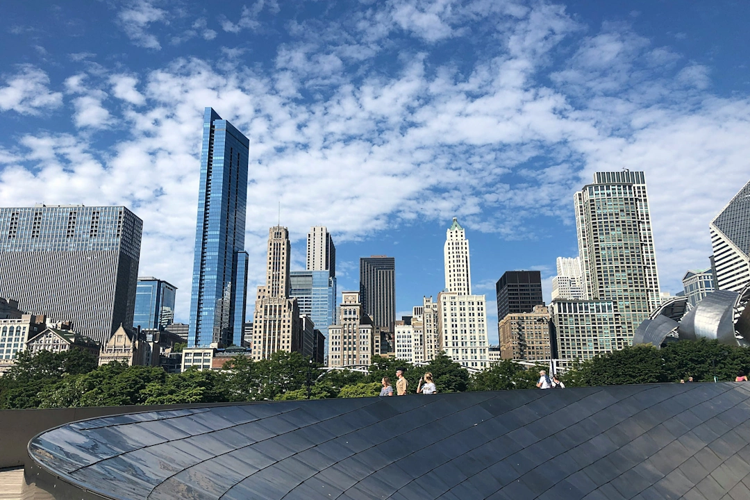 Downtown Chicago cityscape viewed from Millennium Park, with historic and modern skyscrapers against a partly cloudy sky.