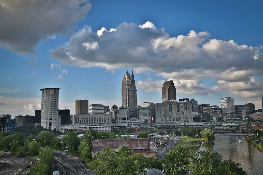 Cleveland skyline featuring Key Tower and Terminal Tower with Cuyahoga River in the foreground under dramatic clouds.