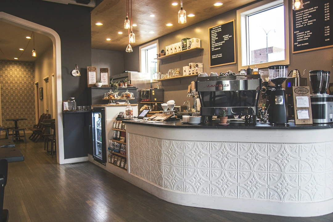 food-and-beverage Modern café counter with an espresso machine, glass pastry case, menu board, and seating area, representing food and beverage