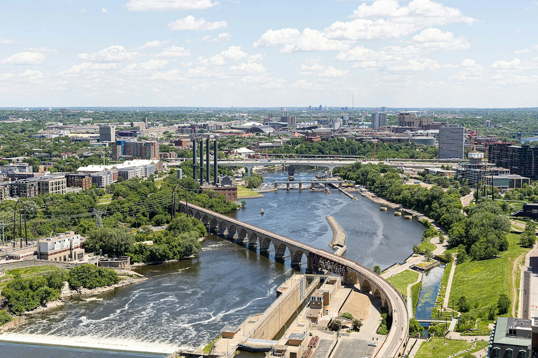 Aerial view of Minneapolis with the Stone Arch Bridge crossing the Mississippi River and city buildings in the background.
