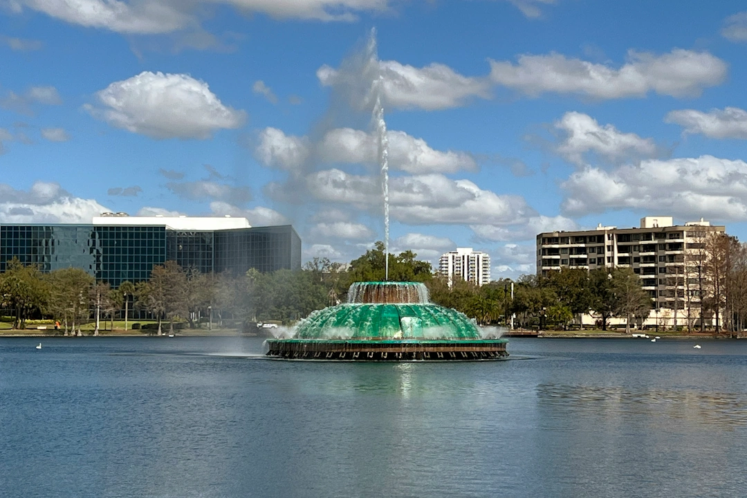 Lake Eola fountain in downtown Orlando, Florida, surrounded by modern buildings and palm trees under blue skies.