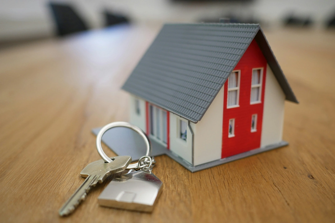 real-estate Small red and gray model house next to a keyring with metal keys placed on a wooden tabletop, representing real estate transactions