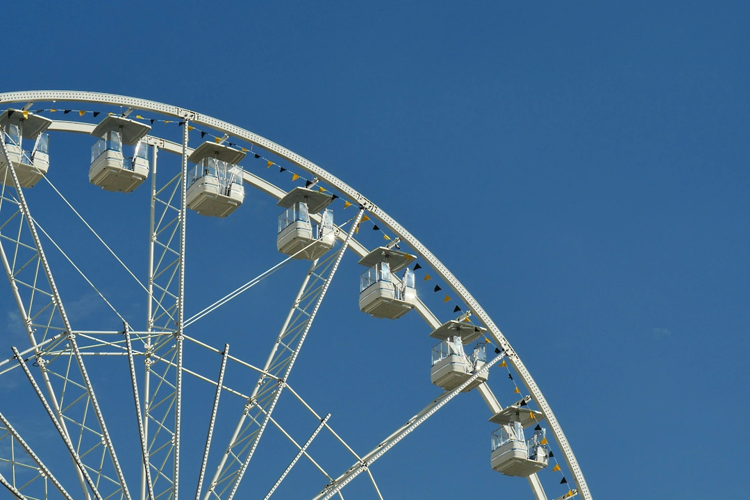 recreation-and-entertainment Partial view of a white Ferris wheel gondola assembly against a clear blue sky at an outdoor amusement attraction