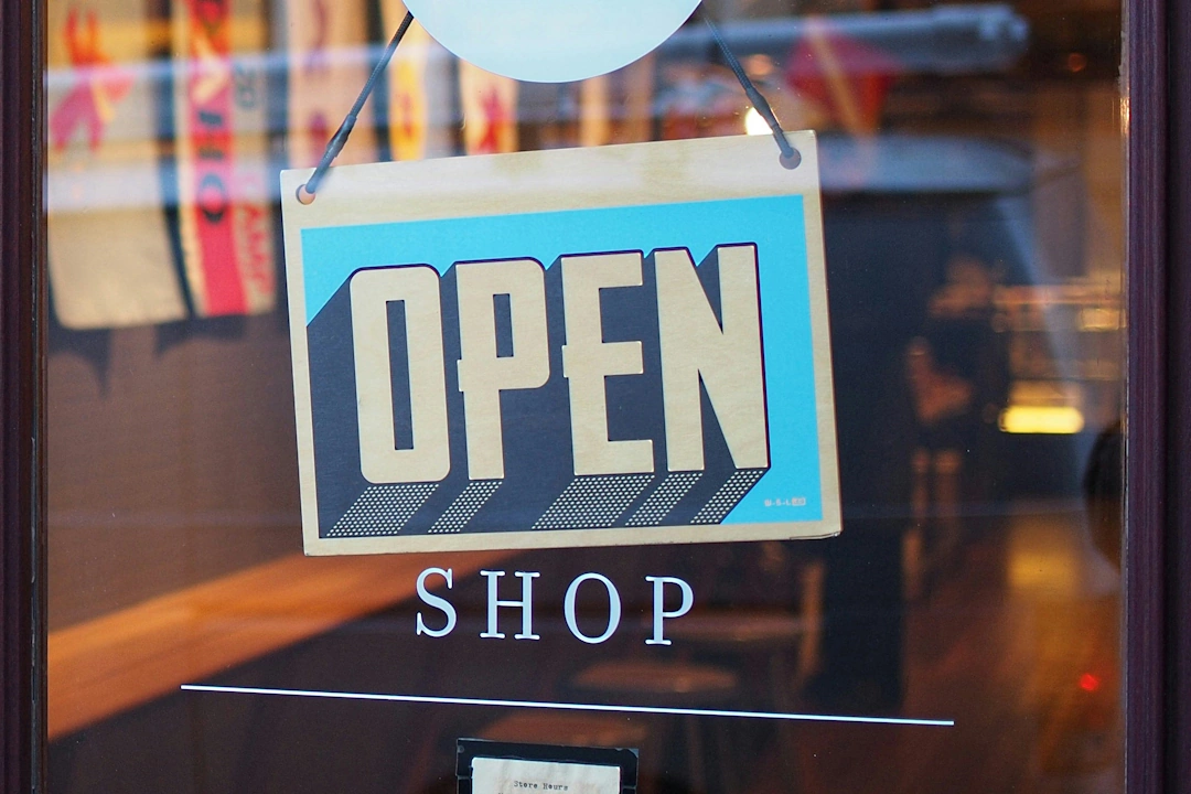retail Glass storefront door with a blue and beige “OPEN” sign hanging above the word “SHOP” on the glass surface