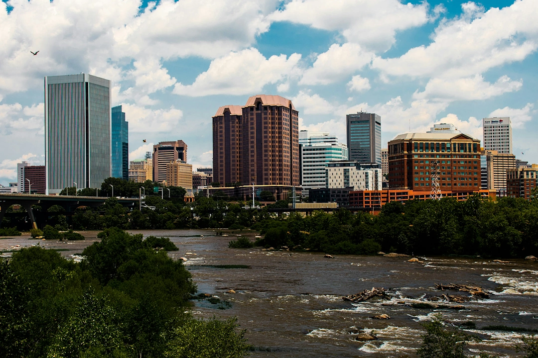 Richmond, Virginia skyline with modern and historic buildings along the James River on a partly cloudy day.